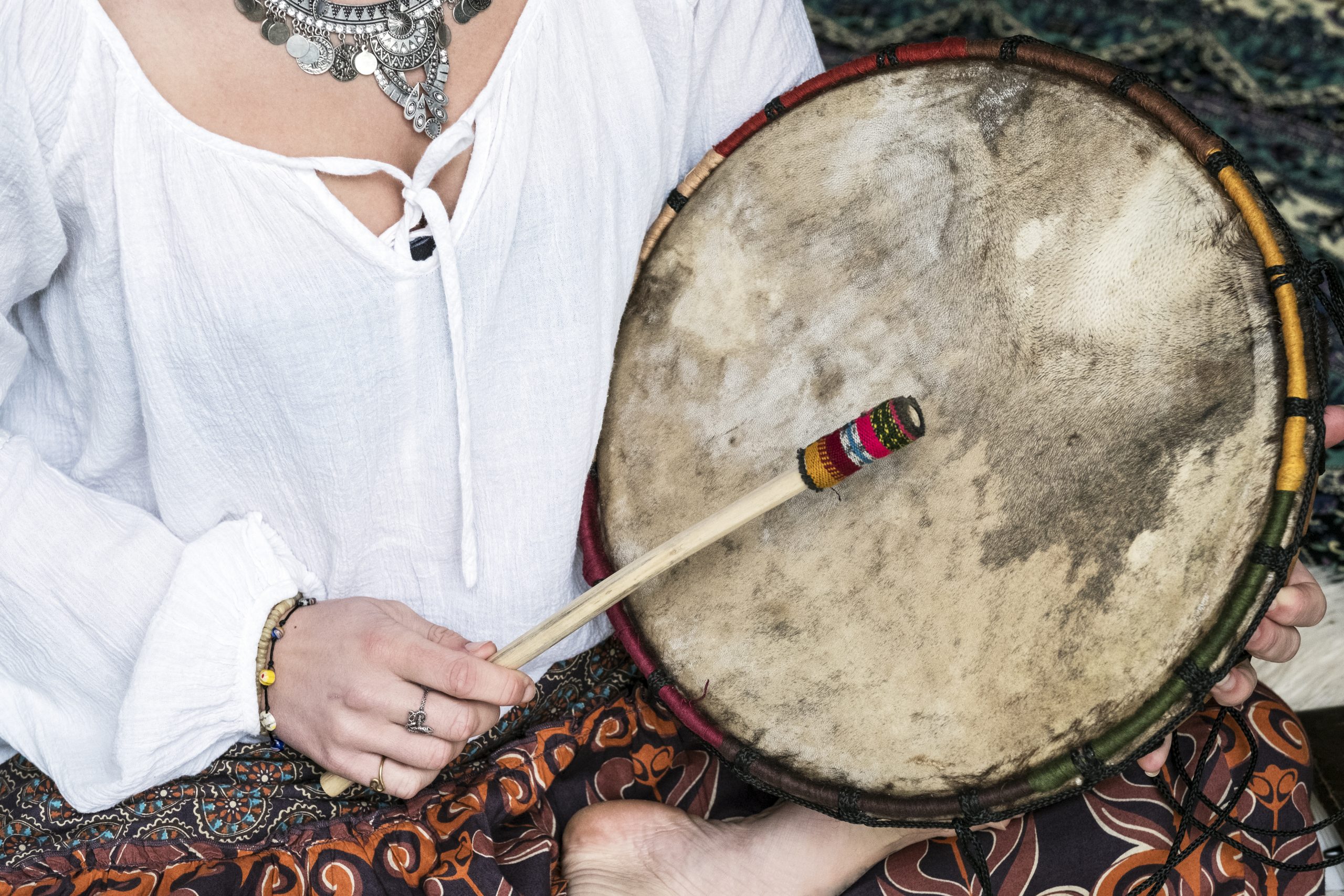 High angle view of woman wearing trousers with floral pattern sitting on shag carpet, holding shaman drum.
